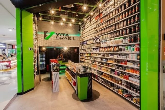 Corredor interno de uma loja VitaBrasil, com prateleiras altas dos dois lados cheias de potes e caixas de marcas diferentes.